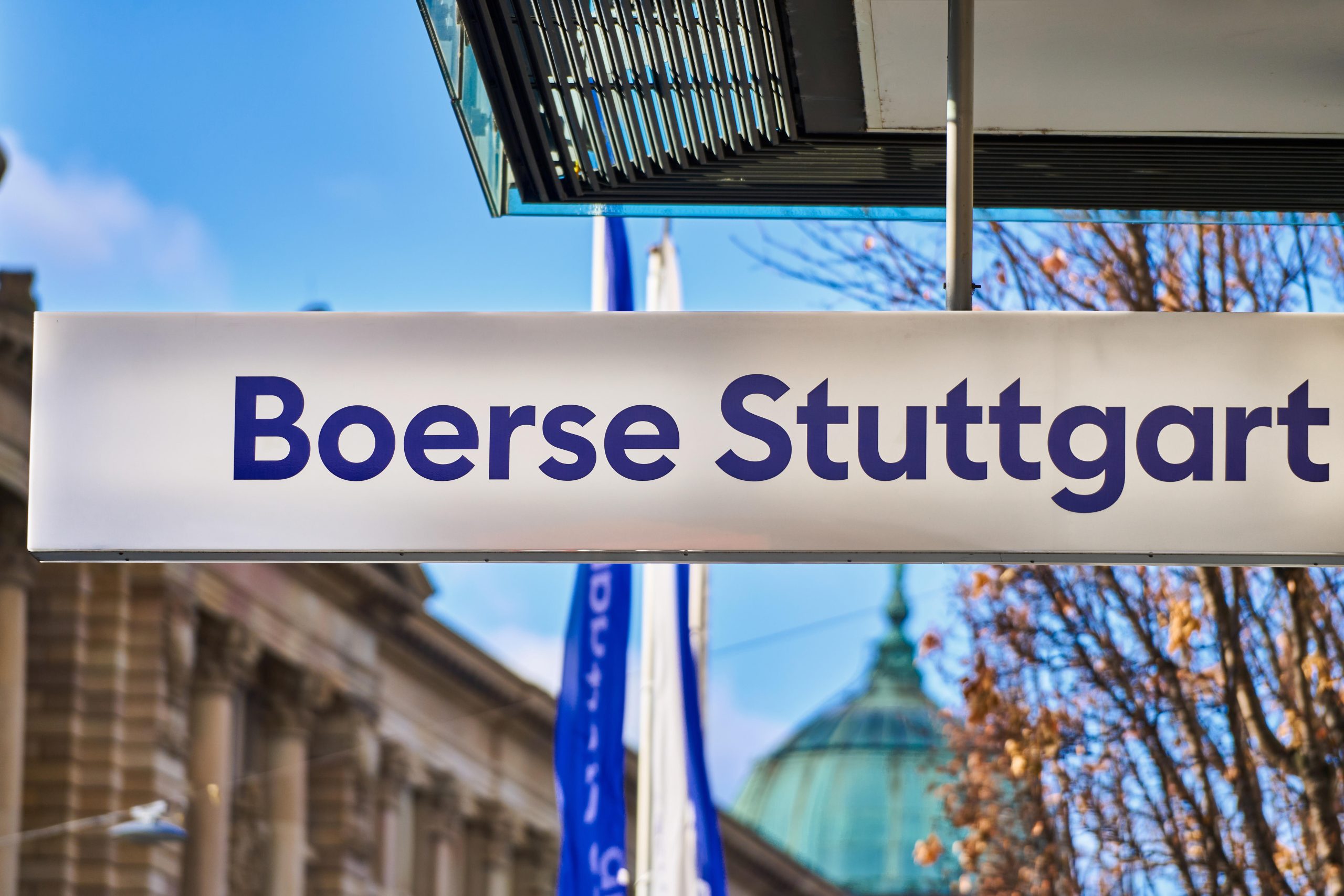 Krypto-Zugang für Investoren: Trever integriert Boerse Stuttgart Digital Ein Schild der Börse Stuttgart ist im Freien zu sehen, mit einem modernen Gebäude und einer Kuppel im Hintergrund.