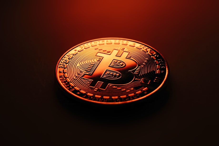 Eine Nahaufnahme einer physischen Bitcoin-Münze mit dem ikonischen Bitcoin-Symbol, beleuchtet von einem orange-roten Licht auf einem dunklen Hintergrund.