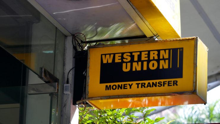 western-union-solana-stablecoin Ein gelb-schwarzes Western Union Money Transfer-Schild ist an der Außenseite eines Gebäudes neben einer Glastür angebracht und weist auf moderne Dienstleistungen wie Stablecoin-Zahlungen neben traditionellen Überweisungen hin.