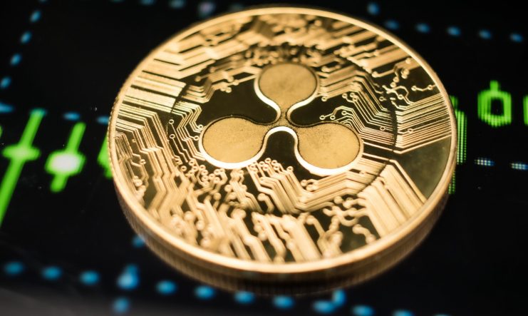 Nahaufnahme einer goldenen XRP-Kryptowährungsmünze auf einem digitalen Bildschirm, der grüne Finanzdiagrammlinien anzeigt.
