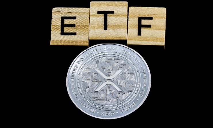 Eine glänzende XRP-Münze ist unter drei Holzkacheln platziert, die ETF auf einem schwarzen Hintergrund buchstabieren.