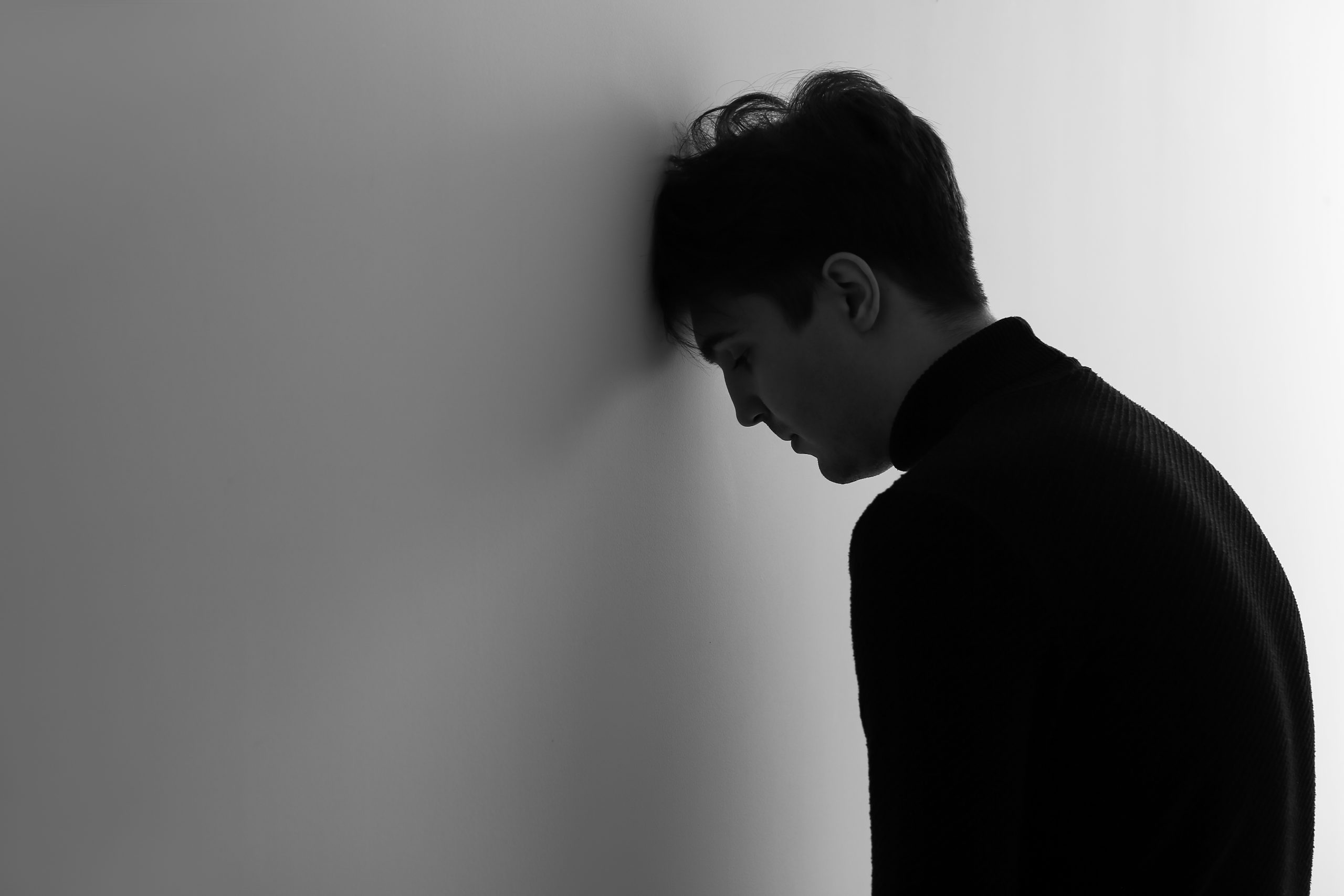 Eine Person steht vor einer leeren Wand und stützt ihre Stirn dagegen. Die Beleuchtung erzeugt einen Silhouetteneffekt, der ihre düstere Haltung unterstreicht - vielleicht belastet von Gedanken an Bitcoin oder Euro-Verluste.