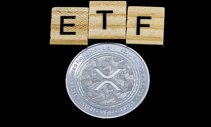 Eine silberne XRP-Münze sitzt unter hölzernen Buchstabenkacheln, auf denen "ETF" steht, und unterstreicht das wachsende Interesse an XRP-basierten ETF-Produkten auf schwarzem Hintergrund.