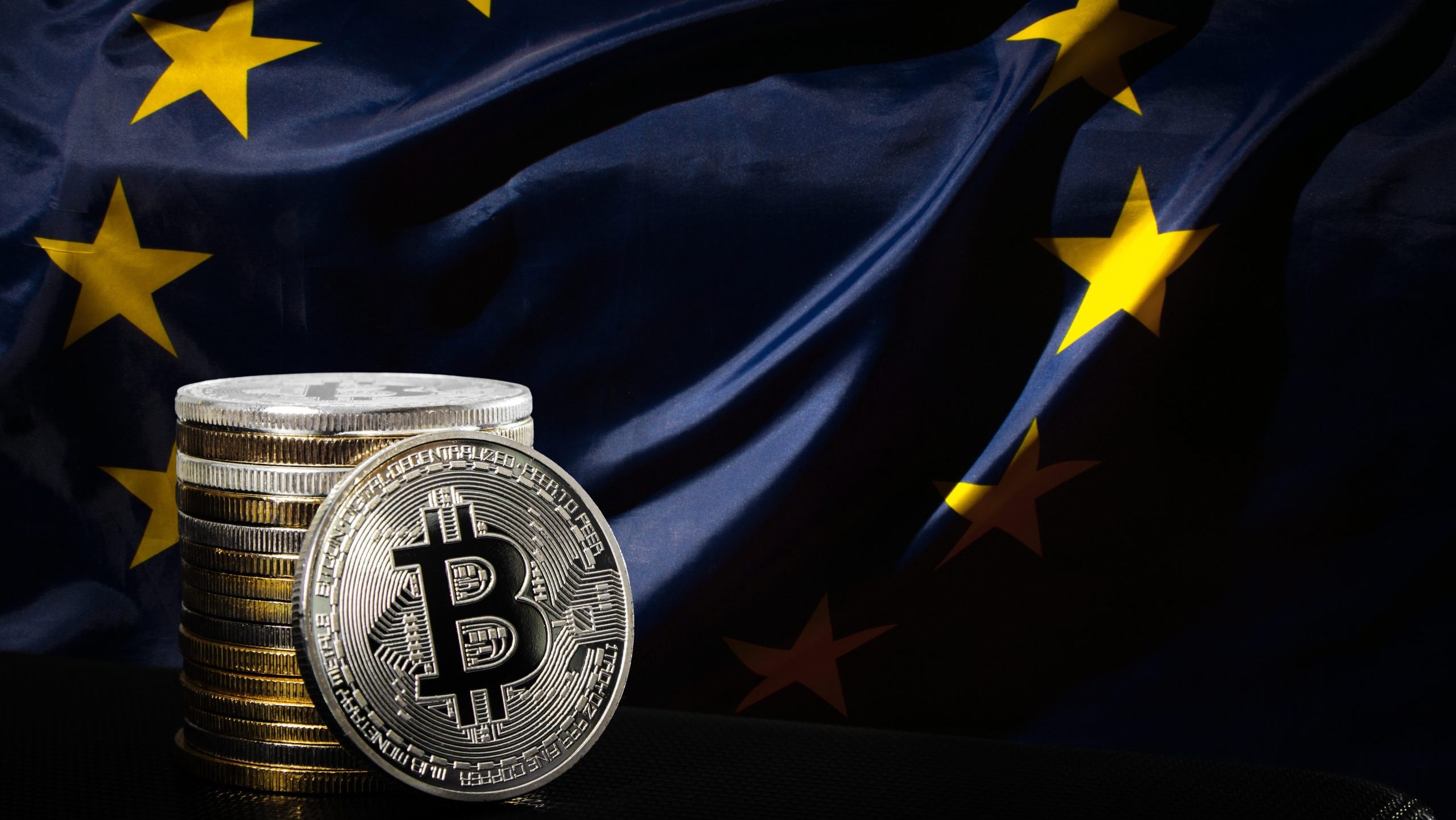 Stapel physischer Bitcoin-Münzen vor einer entfalteten Flagge der Europäischen Union, die den Markteintritt von Coinmerce in Deutschland und die Bereitschaft für die kommenden MiCAR-Lizenzbestimmungen symbolisiert.