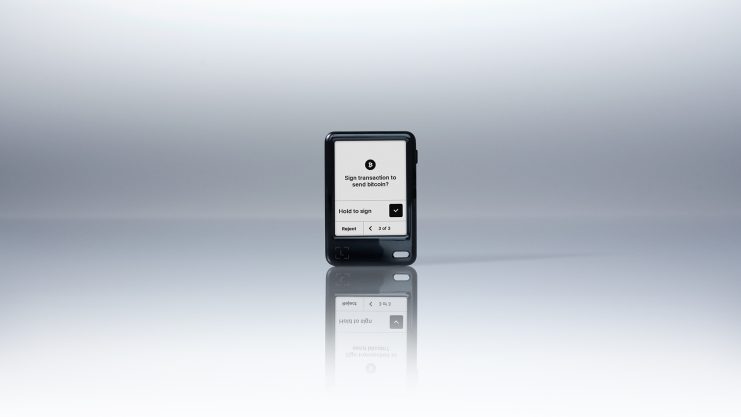 Der Ledger Nano Gen5 mit einem Bildschirm zeigt eine Aufforderung zur Unterzeichnung einer Transaktion an, mit Aktionstasten und einem minimalen, reflektierenden Hintergrund.