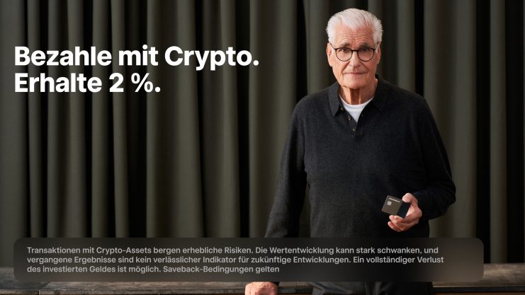 Ein älterer Mann mit Brille steht in einem Haus und hält ein kleines Gerät. Der Text neben ihm lautet: Bezahle mit Crypto über Trade Republic. Erhalte 2 %. Vorhang im Hintergrund, zusätzlicher Disclaimer-Text darunter.