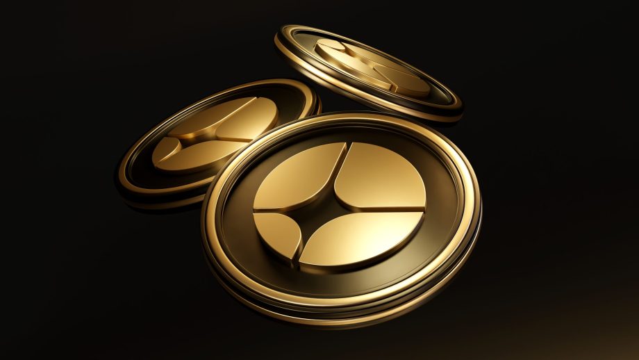 Drei goldglänzende ASTER-Münzen mit einem kreisförmigen geometrischen Muster sind auf einem dunklen Hintergrund abgebildet.