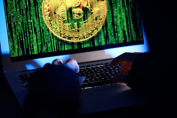 Hände, die auf einer Laptop-Tastatur tippen, während auf dem Bildschirm ein großes Bitcoin-Symbol und ein grüner Binärcode angezeigt werden, der Verbindungen zu DeFi-Innovationen hervorhebt.