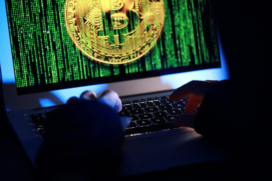 Hände, die auf einer Laptop-Tastatur tippen, während auf dem Bildschirm ein großes Bitcoin-Symbol und ein grüner Binärcode angezeigt werden, der Verbindungen zu DeFi-Innovationen hervorhebt.