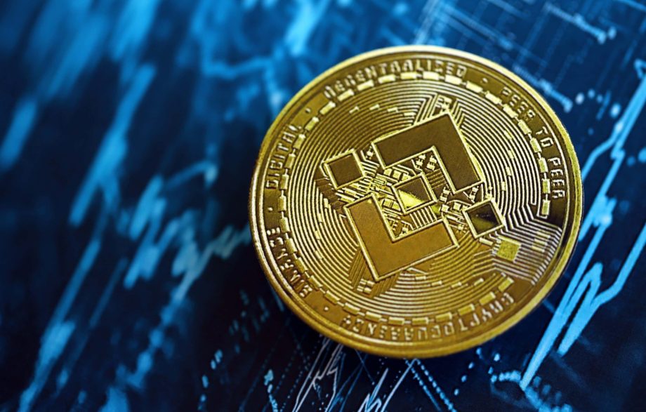 Eine goldene BNB Binance-Münze ruht auf einem blauen Hintergrund, auf dem Finanzcharts und Datengrafiken zu sehen sind.