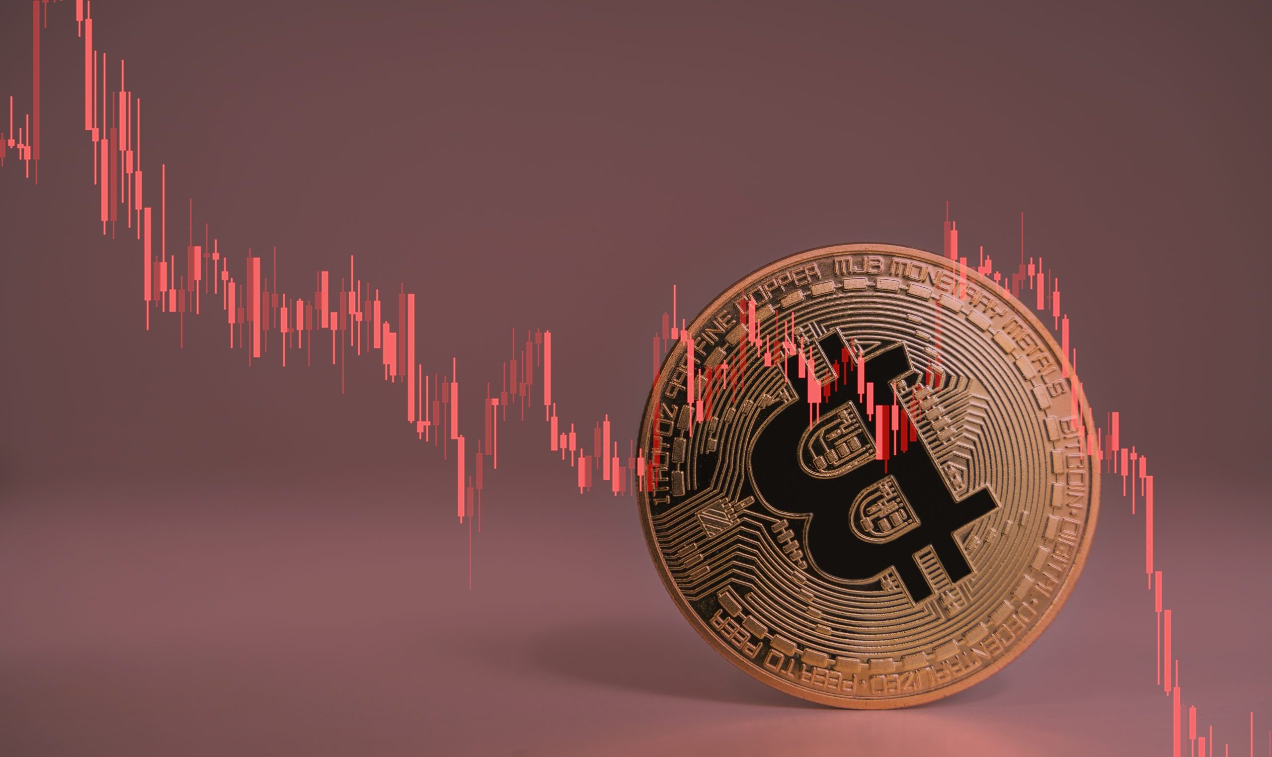 Eine Bitcoin-Münze taumelt, dazu ein abstürzender Chart in rot