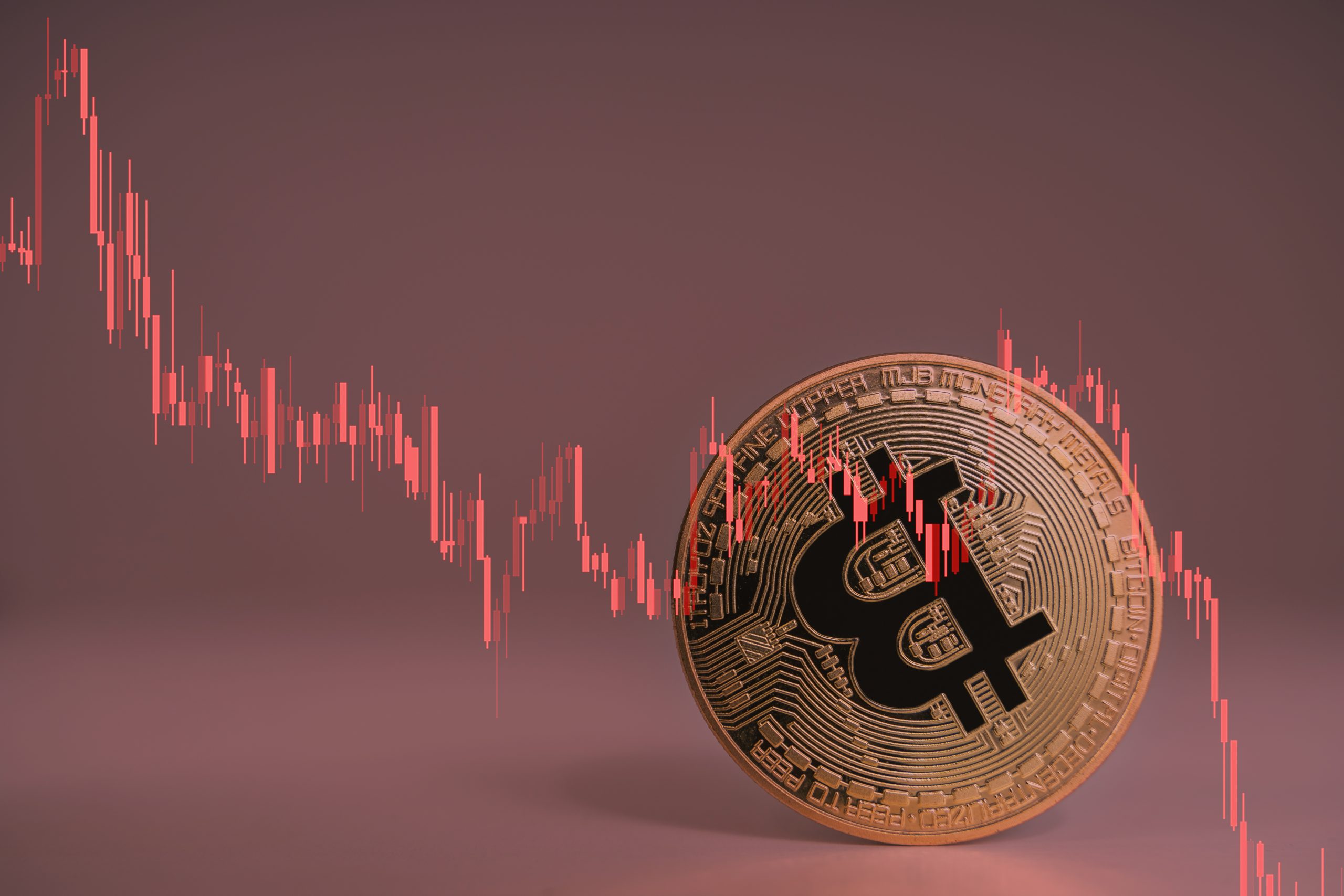 Eine Bitcoin-Münze taumelt, dazu ein abstürzender Chart in rot