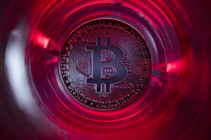 Nahaufnahme einer physischen Bitcoin-Münze unter roter Beleuchtung, die das Bitcoin-Symbol und das komplizierte Schaltkreisdesign hervorhebt.