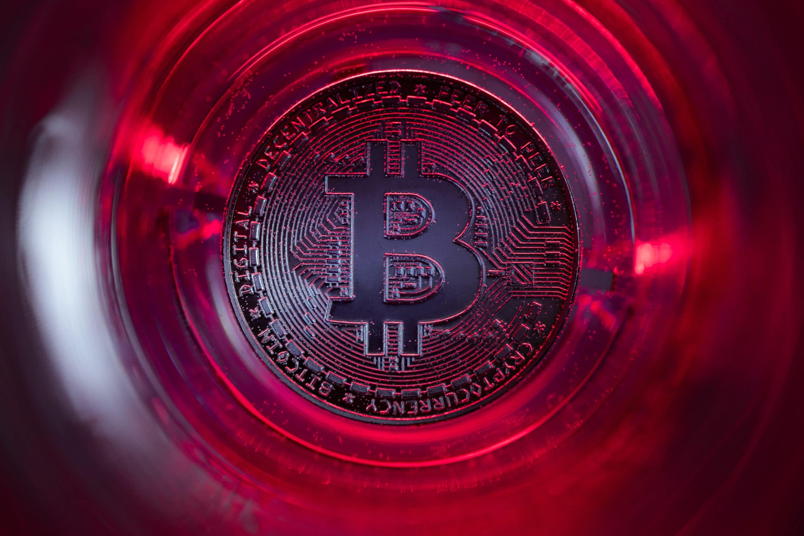 Nahaufnahme einer physischen Bitcoin-Münze unter roter Beleuchtung, die das Bitcoin-Symbol und das komplizierte Schaltkreisdesign hervorhebt.