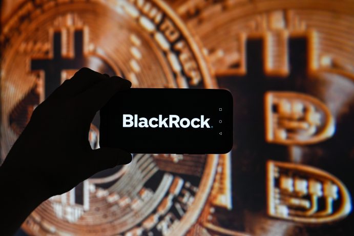 Eine Hand hält ein Smartphone mit Blackrock-Logo, im Hintergrund einige vergrößerte Bitcoin-Münzen