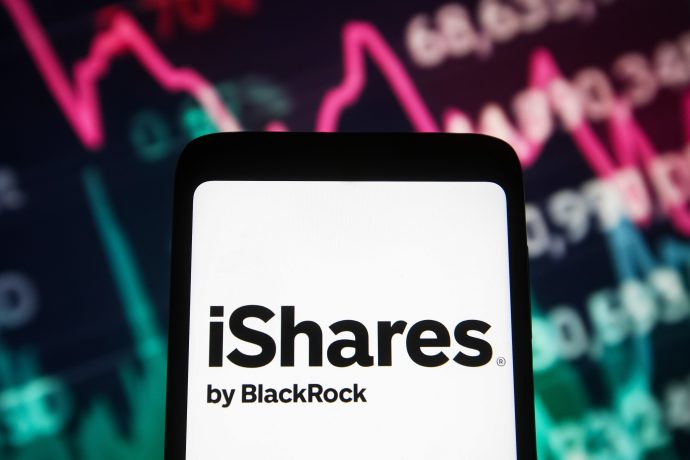 Auf einem Smartphone ist das iShares by BlackRock-Logo zu sehen, mit einem unscharfen Hintergrund, der eine Grafik mit Börsendaten und Bitcoin-Trends zeigt, die durch rosa und grüne Linien hervorgehoben werden.
