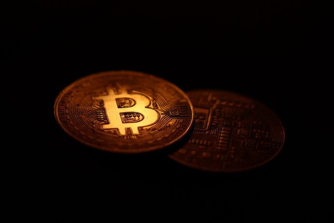 Zwei physische Bitcoins ruhen auf einer dunklen Oberfläche. Auf dem einen prangt das Bitcoin-Logo, während der andere verschlungene, kreislaufartige Muster aufweist.