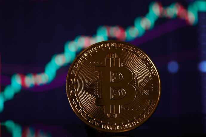 Ein physischer Bitcoin-Token steht vor einem verschwommenen Diagramm, das eine Aufwärtsbewegung zeigt und die Wertschwankungen der Kryptowährung Bitcoin symbolisiert.