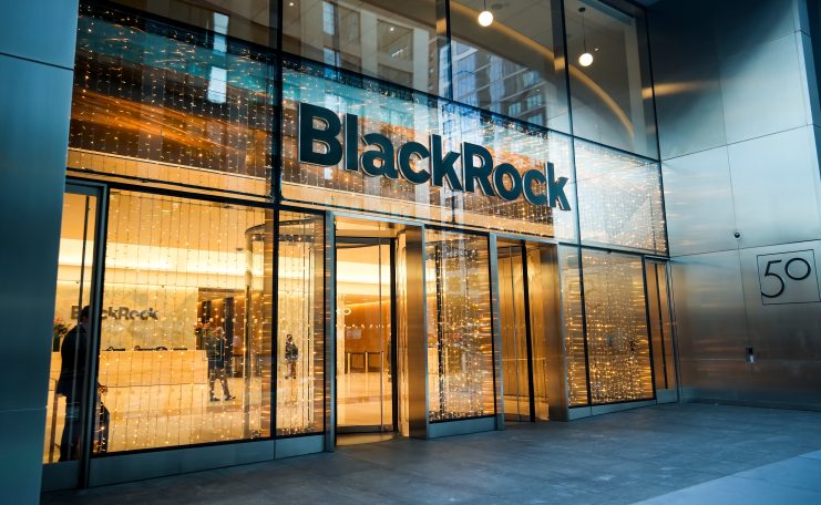Eingang zu einem modernen Bürogebäude mit großen Glastüren und einem Schild mit der Aufschrift BlackRock über dem Eingang, beleuchtet von Innenleuchten - ein Zentrum für Gespräche über Investitionen und Kryptowährungen.