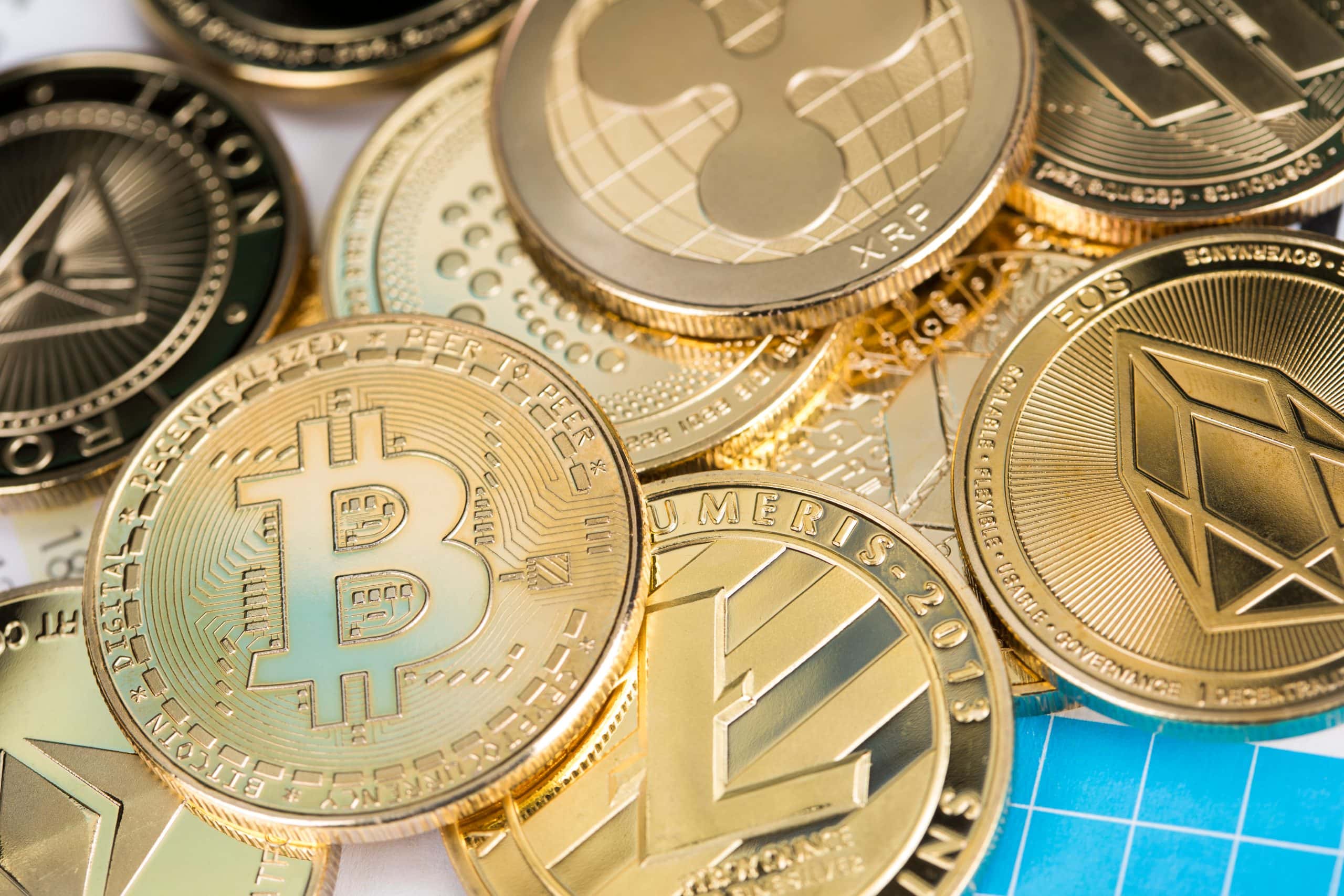 Verschiedene physische Münzen, die verschiedene Blockchain-basierte Kryptowährungen repräsentieren, darunter Bitcoin, Ripple und Ethereum, in einer Nahaufnahme.