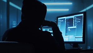 Eine dunkel gekleidete Person sitzt vor einem Laptop