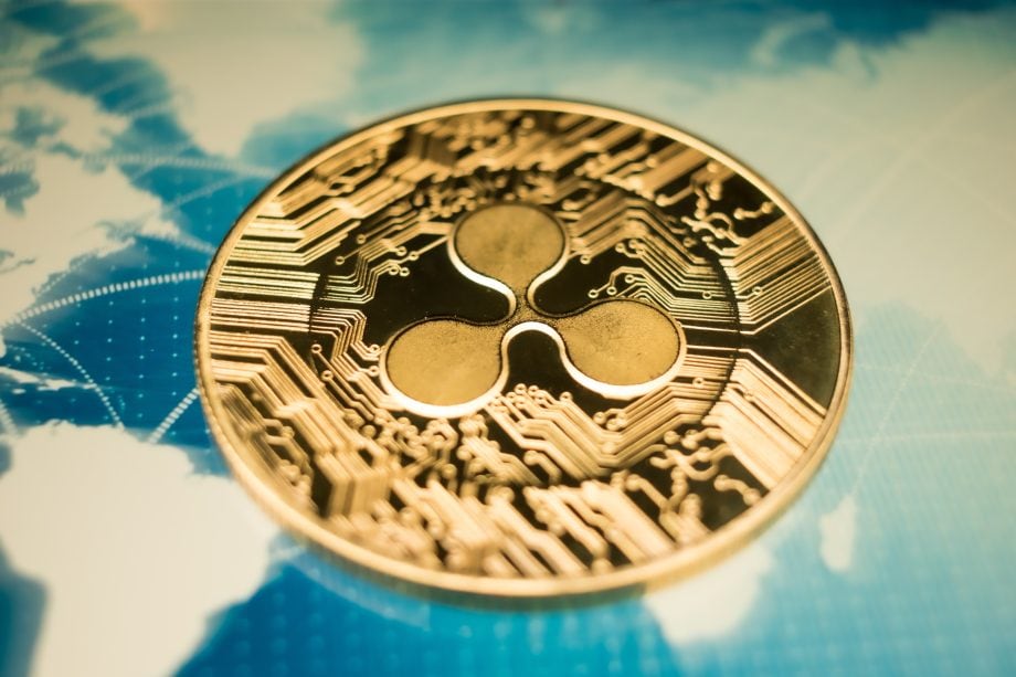Nahaufnahme einer goldenen XRP-Kryptowährungsmünze auf einem blauen Weltkartenhintergrund mit digitalen Linien.
