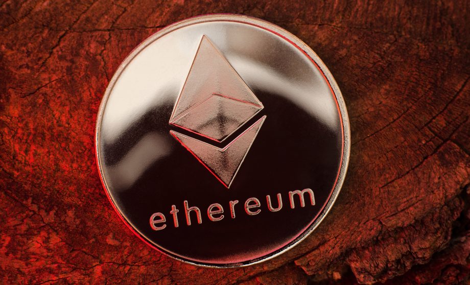 Eine silberne Ethereum-Münze mit dem Ethereum-Logo und dem eingravierten Wort "Ethereum" ruht auf einer strukturierten rotbraunen Holzoberfläche.