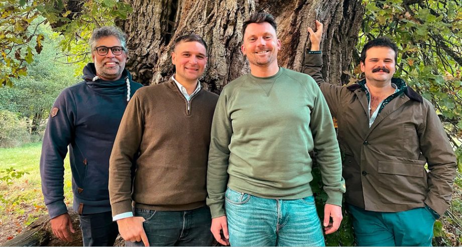 Vier Männer stehen im Freien vor einem großen Baum und lächeln in die Kamera, als ob sie gemeinsam ein erfolgreiches Tokenisierungsprojekt feiern würden.