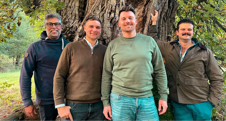 Vier Männer stehen im Freien vor einem großen Baum und lächeln in die Kamera, als ob sie gemeinsam ein erfolgreiches Tokenisierungsprojekt feiern würden.