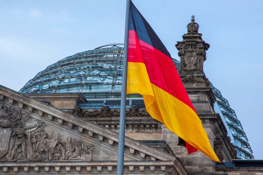 Die deutsche Flagge vor dem Reichstagsgebäude in Berlin mit seiner Glaskuppel und der detaillierten Steinfassade symbolisiert Transparenz - ähnlich wie die Offenheit, die von Krypto-Enthusiasten propagiert wird.