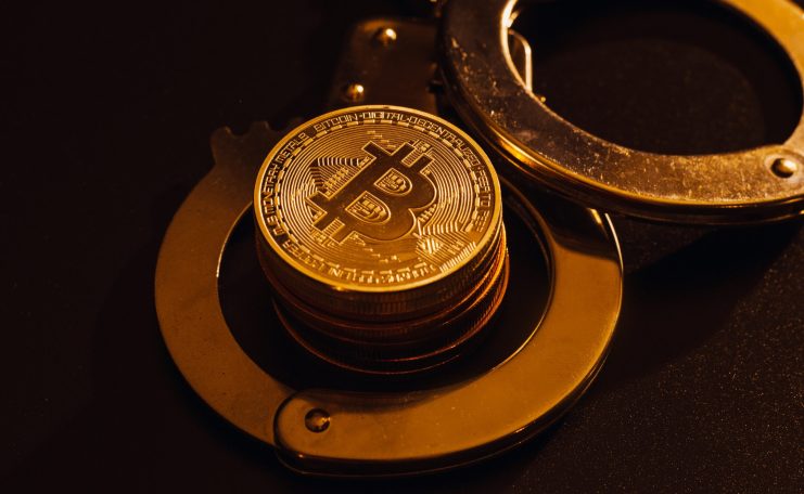Ein Stapel Bitcoin-Münzen sitzt in einem offenen Paar Metallhandschellen auf einer dunklen Oberfläche und symbolisiert die Spannung zwischen Krypto-Freiheit und Regulierung.