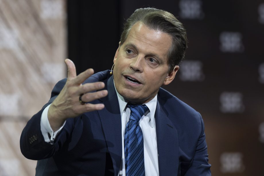 Ein Mann in Anzug und Krawatte gestikuliert mit seiner Hand, während er auf einer Veranstaltung über Bitcoin-Mining spricht und ein Headset-Mikrofon trägt.