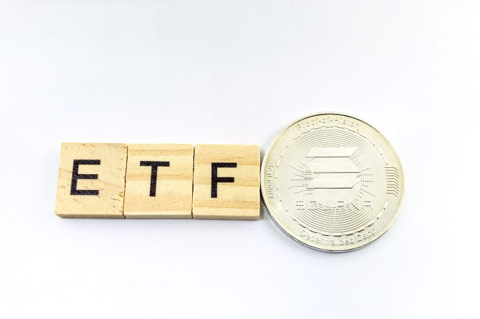 Holzblöcke mit der Aufschrift ETF stehen neben einer silbernen Kryptowährungsmünze, die auf den Solana-Spot-ETF verweist, auf einem weißen Hintergrund.