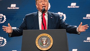 Ein Mann im Anzug und mit roter Krawatte spricht an einem Podium mit dem Siegel des Präsidenten der Vereinigten Staaten über Bitcoin vor einem blauen Hintergrund mit Logos des Farm Bureau.