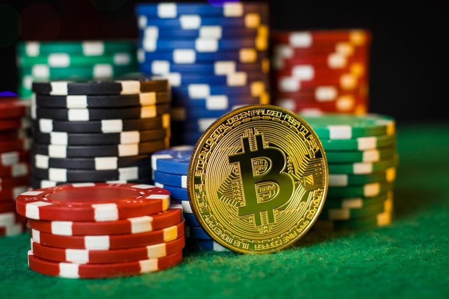 Eine goldene Bitcoin-Münze steht inmitten von Stapeln bunter Pokerchips auf einer grünen Filzoberfläche und erinnert an ein spannendes Krypto-Casino.