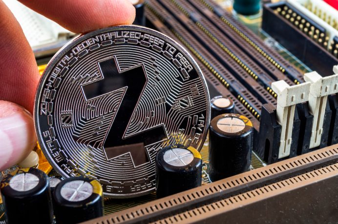 Eine Hand hält eine Münze der Kryptowährung Zcash über einer Computer-Hauptplatine und unterstreicht damit die Verbindung zwischen Zcash und hochmodernen elektronischen Komponenten.