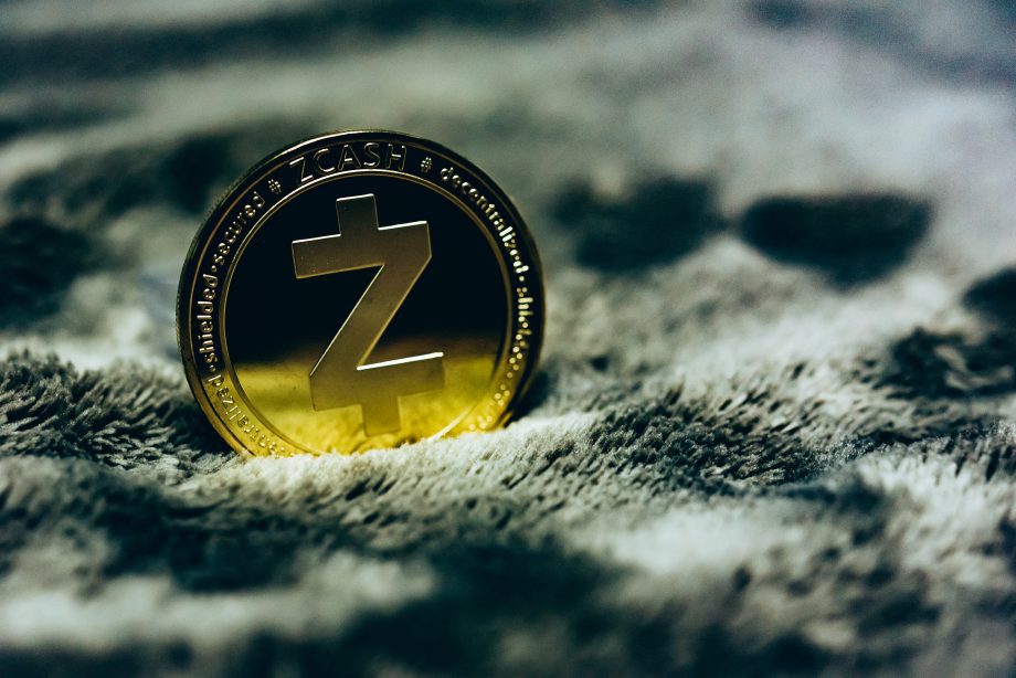 Eine goldene Zcash-Münze steht aufrecht auf einer strukturierten, grauen Oberfläche und symbolisiert den wachsenden Einfluss von Zcash in der Welt der Kryptowährungen.