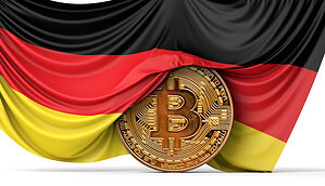 Das Bild zeigt eine Bitcoin-Münze vor der deutschen Flagge