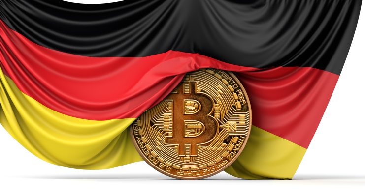Das Bild zeigt eine Bitcoin-Münze vor der deutschen Flagge