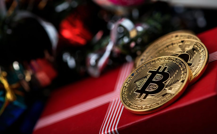 Zwei Bitcoin-Münzen liegen auf einem verpackten Geschenk neben Christbaumkugeln.
