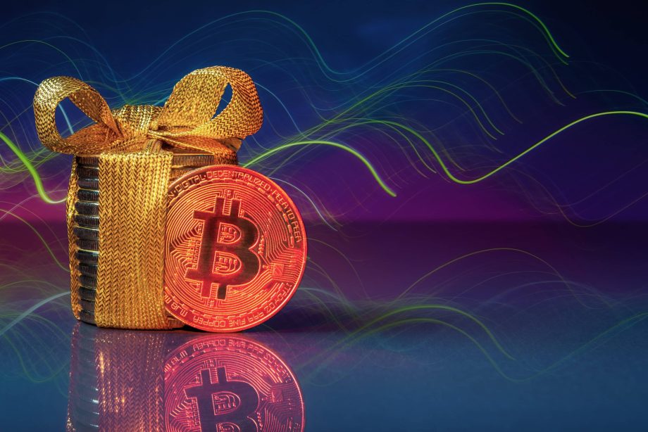 Bitcoin mit einem goldenen Geschenk und einem blau-lila Hintergrund.