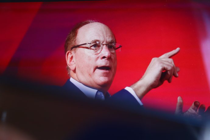 BlackRock CEO Larry Fink gestikuliert mit seiner rechten Hand, während er vor einem roten Hintergrund über die Bitcoin-ETFs von BlackRock spricht.