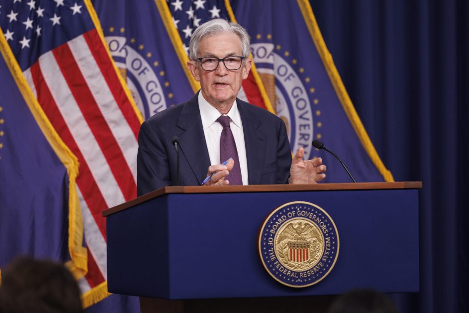 Ein Mann im Anzug steht vor einem Rednerpult der Federal Reserve. Im Hintergrund sind US-Flaggen.