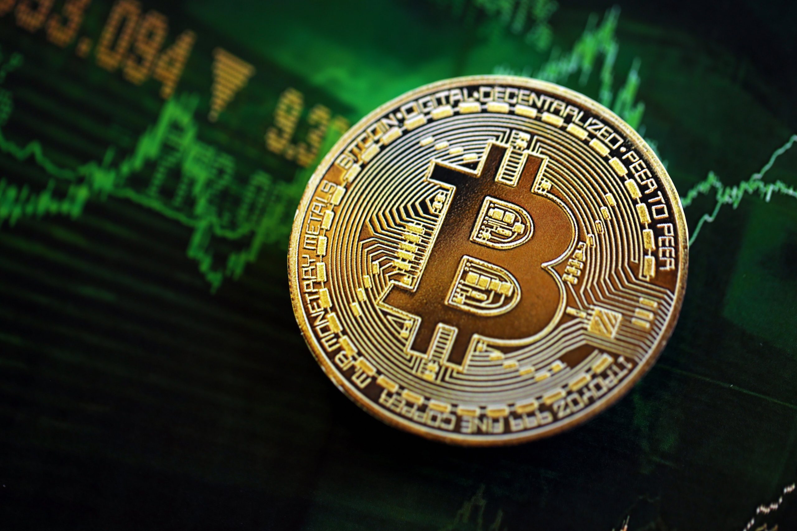Eine goldfarbene Bitcoin-Münze ruht auf einem Bildschirm mit grünen Finanzgraphen und Zahlen, die den Kryptowährungshandel und die Marktaktivitäten im November symbolisieren.