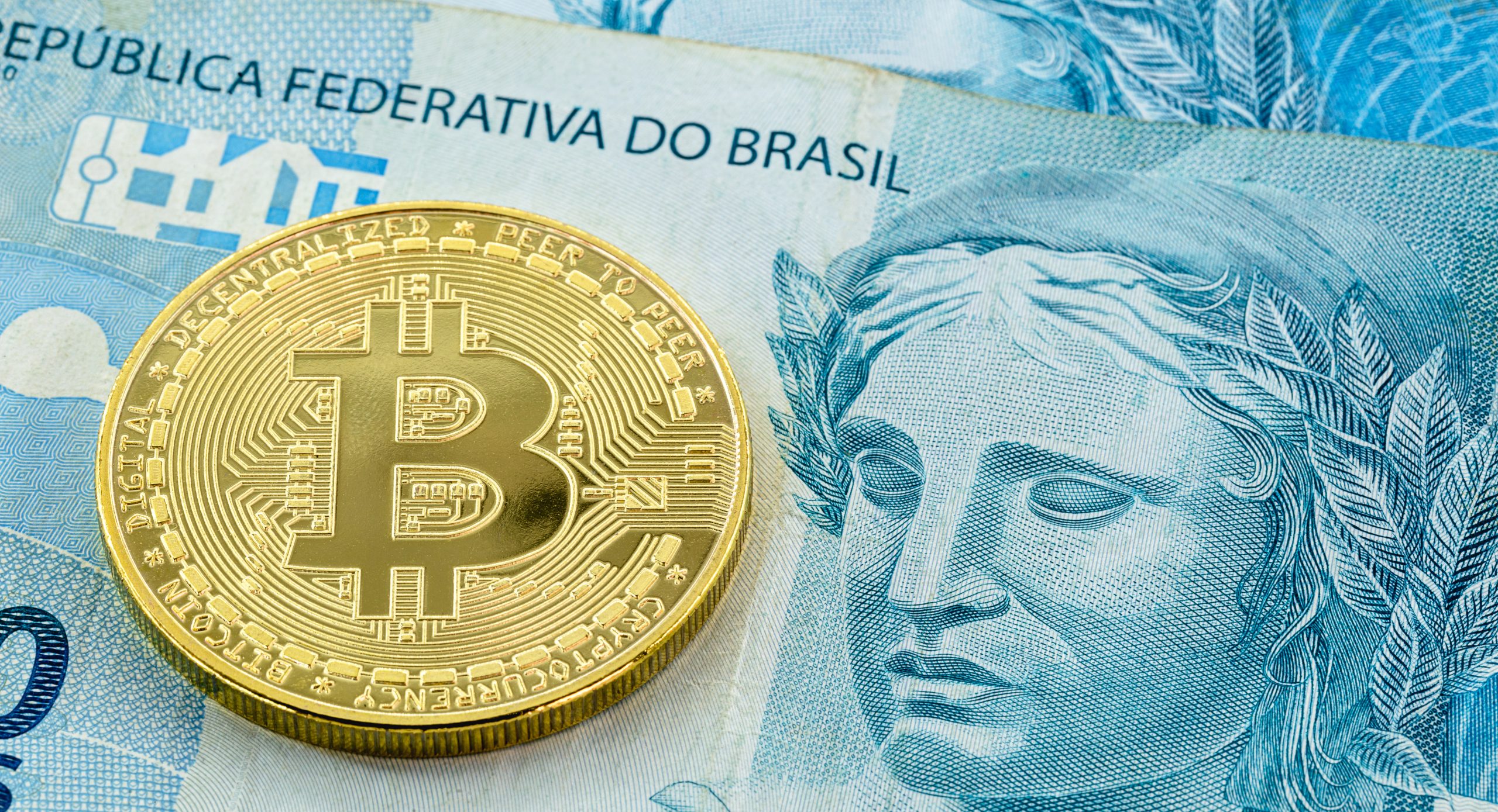 Eine Bitcoin-Münze liegt auf einem brasilianischen Geldschein