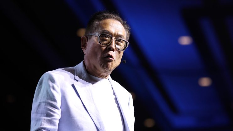 Ein asiatischstämmiger Mann steht auf einer Bühne. Er trägt ein weißes Sakko und eine Brille