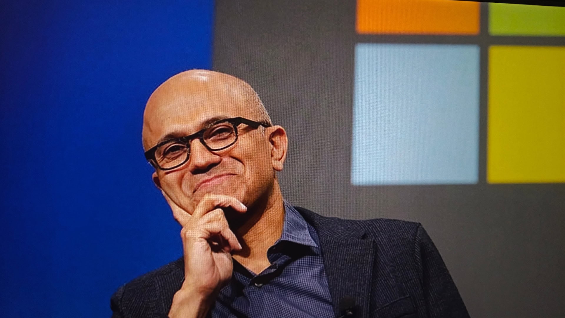 Microsoft-CEO Satya Nadella auf einer Bühne vor einem Bildschirm mit dem Microsoft Logo.