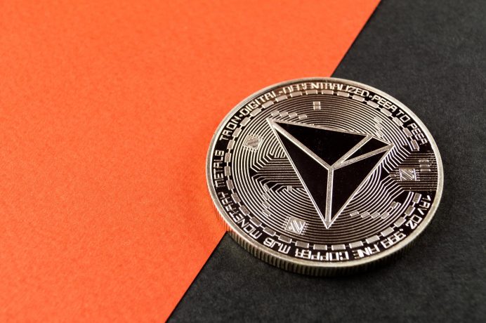 Eine Tron-Kryptowährungsmünze sitzt prominent auf einem diagonalen orangen und schwarzen Hintergrund