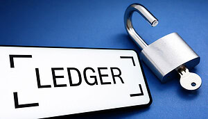 Das Logo von Ledger auf einem Smartphone-Bildschirm. Daneben ist ein geöffnetes Vorhängeschloss zu sehen.