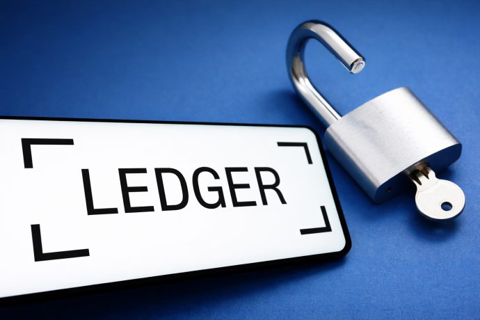 Das Logo von Ledger auf einem Smartphone-Bildschirm. Daneben ist ein geöffnetes Vorhängeschloss zu sehen.